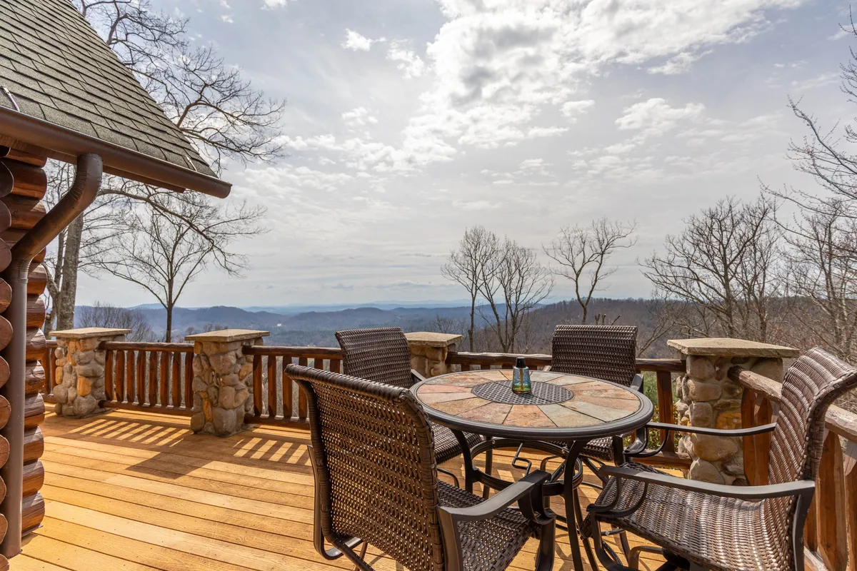 This image presents an outdoor dining area with a wooden table and chairs set on a deck, overlooking a sweeping mountain view. The wooden railing and stone accents ground the scene in rustic authenticity, while the mountains beyond hint at endless outdoor explorations. The setup invites visitors to enjoy meals or morning coffee immersed in the landscape.