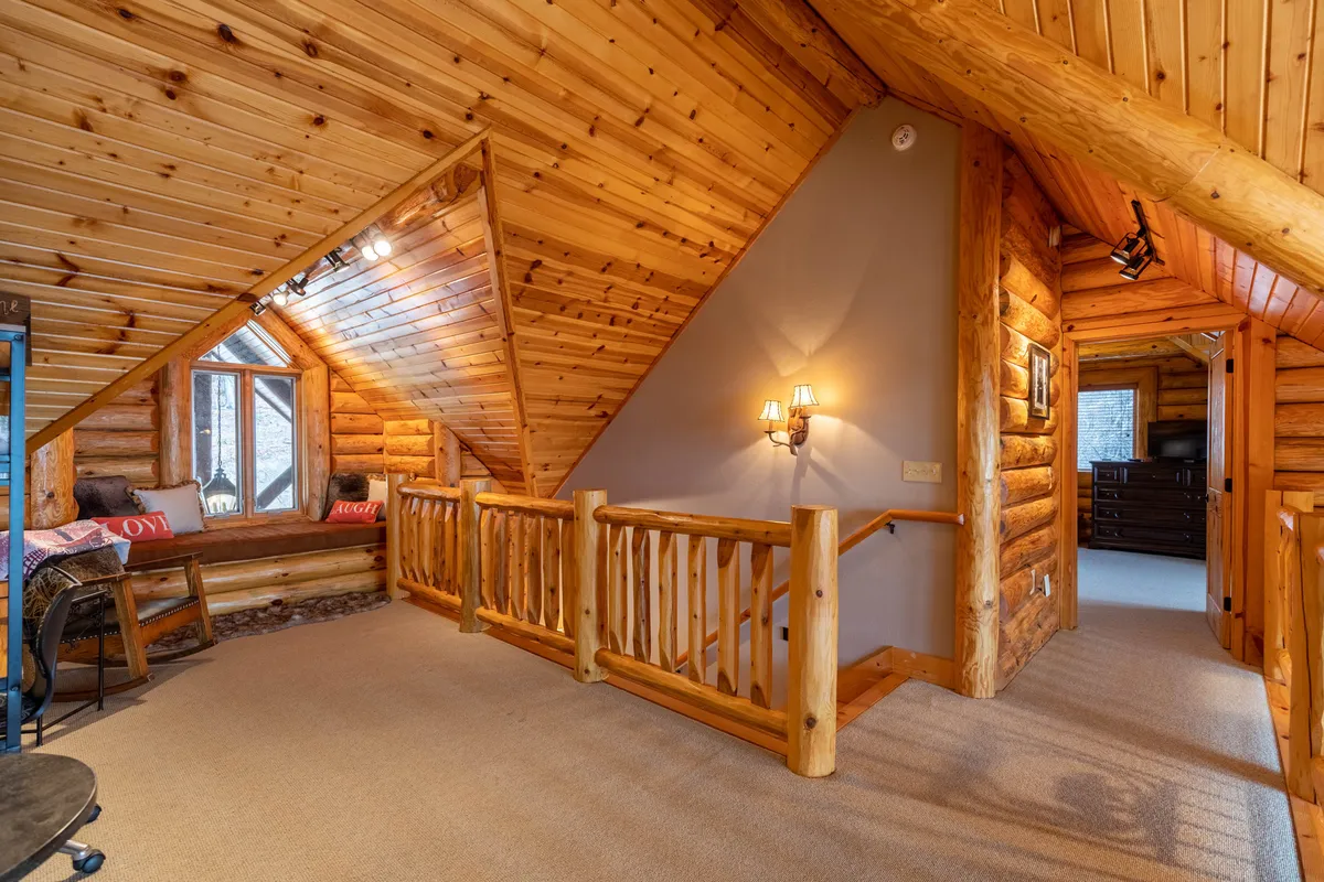 This image captures a rustic seating area with large windows, log railings, and wooden beams. The windows frame the outdoors, allowing guests to observe the changing seasons—spring’s greenery, autumn’s colors, or winter’s snowfall—from the warmth and comfort of the cabin interior.