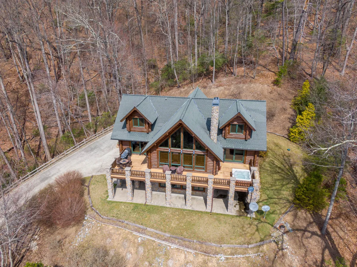 This wide exterior shot features the log cabin’s architecture with large windows, a balcony, and is framed by lush trees. The scene exudes a sense of adventure awaiting just outside, with the balcony and proximity to forested surroundings showcasing the cabin as a literal gateway to outdoor activities.