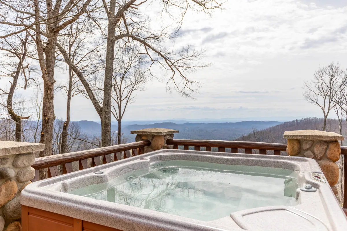 A serene hot tub sits on the deck, overlooking endless mountain ridges framed by bare trees. The tranquil setting is ideal for relaxing soaks, with the open-air environment offering an unobstructed vista—ideal for both sunrise and stargazing.