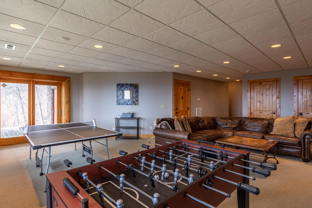 A playful recreation room with both a foosball and ping pong table positioned side by side, a comfortable couch for spectators or players to relax, and rustic wooden doors adding to the cozy, inviting vibe.