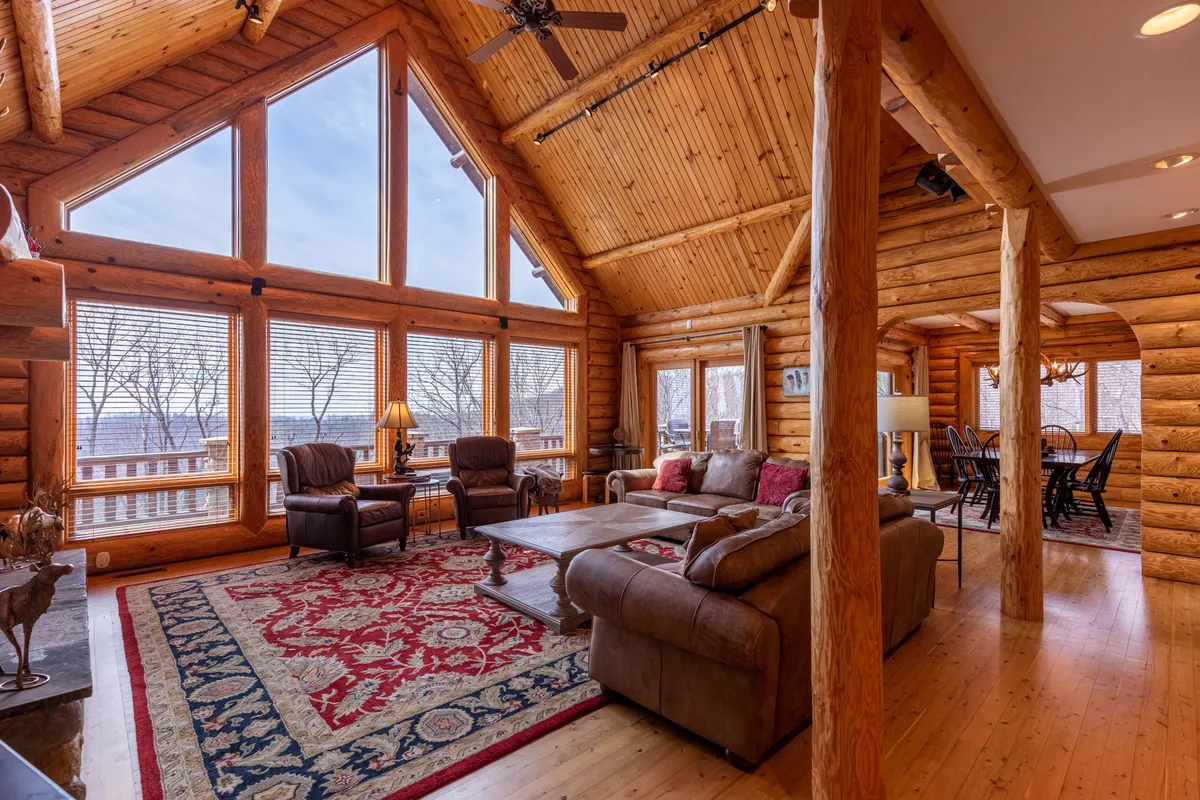 A spacious, warm interior gathering space with a large dining table, comfortable seating area, expansive windows for natural light, and wooden beams overhead. The setup suggests opportunities for board games, group activities, and family-style gatherings.