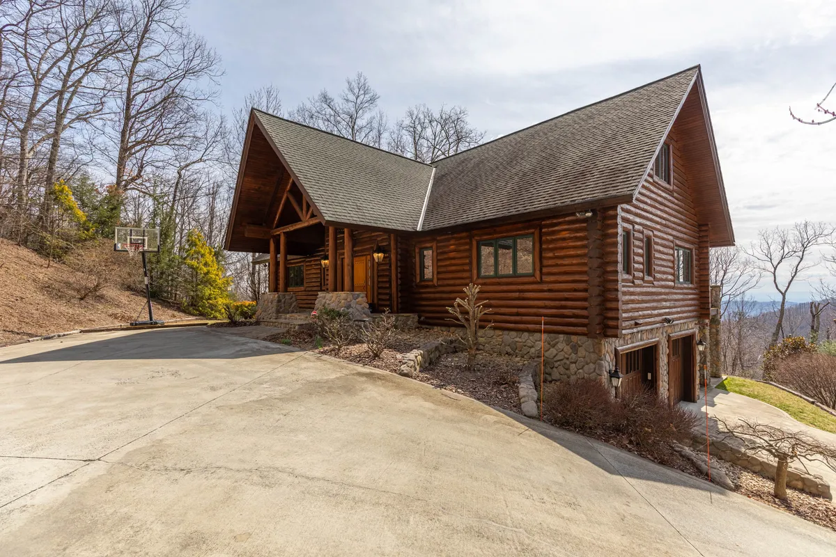 This image displays a welcoming log cabin exterior, complete with a stone pathway, a basketball hoop for friendly games, and lush surrounding trees. The spacious setting suggests ample room for parking and outdoor play, adding a playful, inclusive vibe to the retreat's appeal.